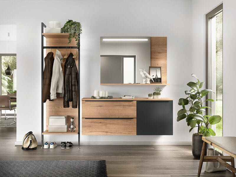 Eine moderne Garderobe in Teilholzoptik mit Ablageflächen, Stauraum und Spiegel in natürlichem Licht. Es hängen Jacken darin und Schuhe stehen unten drunter.