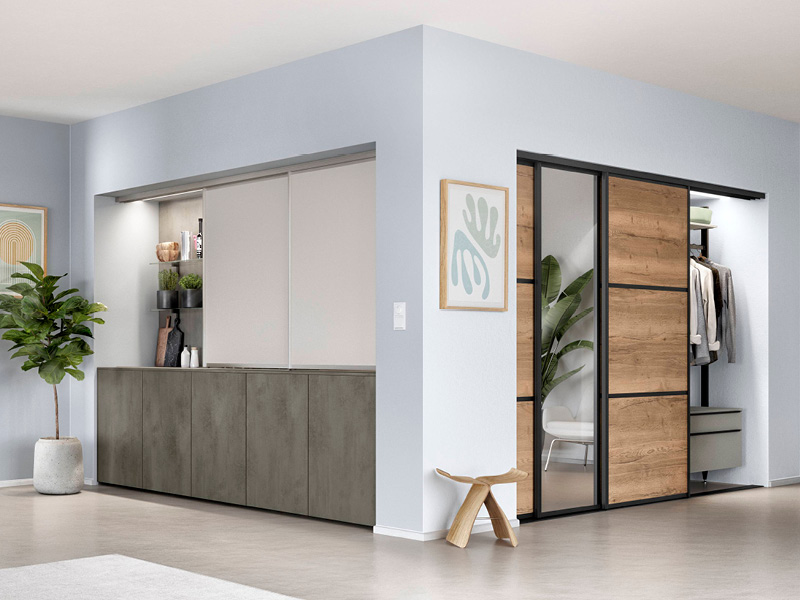 Eine Ecke, die links eine Wohnwand zeigt und rechts eine aufschiebbare Garderobe in modernen Teilholzoptik mit großem bodenlangen Spiegel.