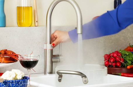 Frauenhand betätigt Temperaturregler am Wasserhahn und erhält kochend heißes Wasser