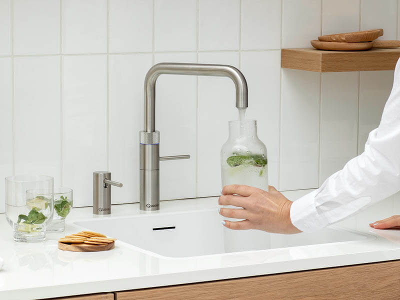 Frau hält Glasflasche unter Quooker-Wasserhahn und erhält kaltes, sprudelndes Wasser