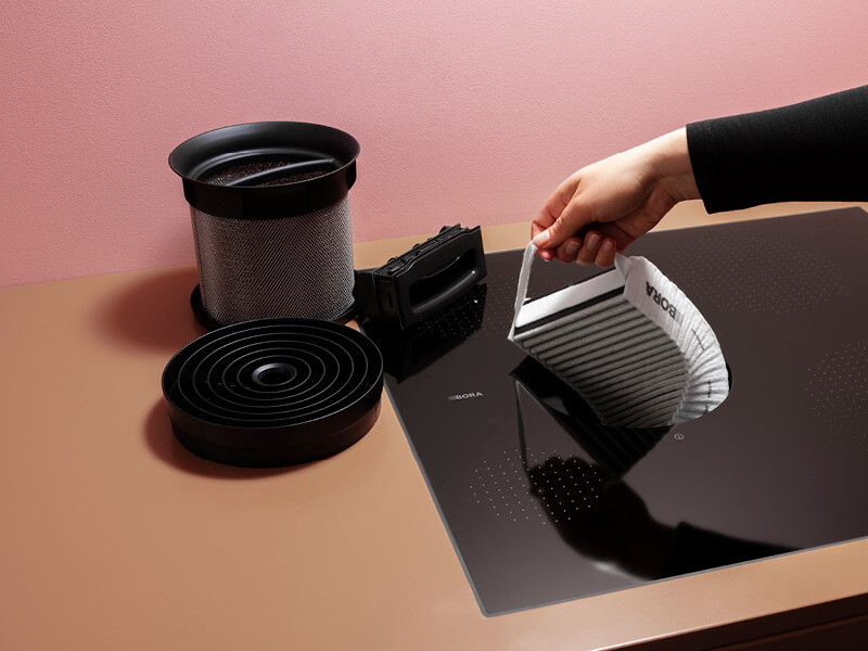 Frauenhand zieht Kohlefilter aus dem Kochfeldabzug von BORA