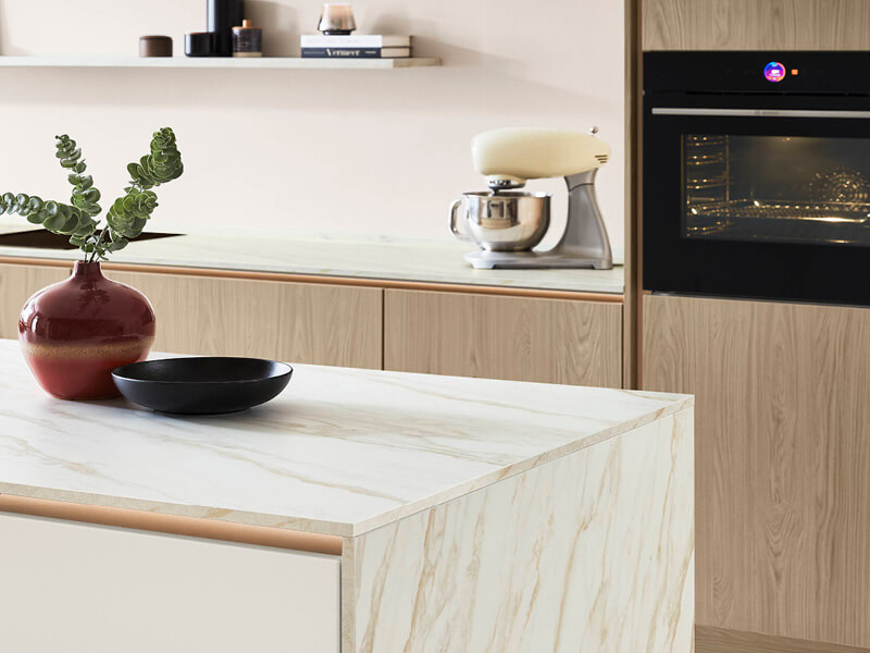 Küche im Materialmix mit Fronten in Holzoptik, Arbeitsflächen in Marmoroptik und bronzefarbenen Griffmulden