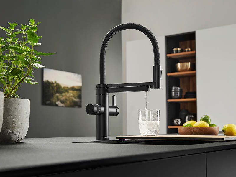 aus schwarzer Küchenarmatur fließt sprudelndes Wasser in Trinkglas