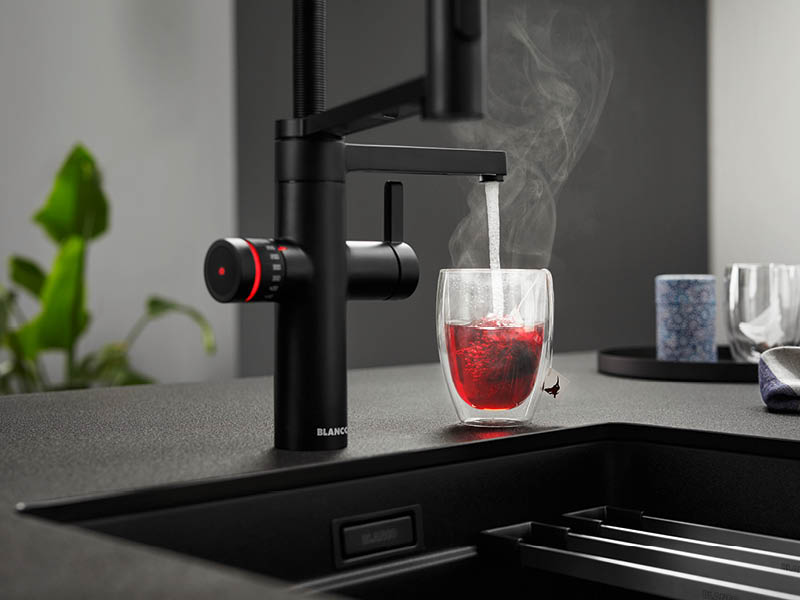 dampfendes, kochend heißes Wasser läuft aus schwarzer Armatur in Teetasse