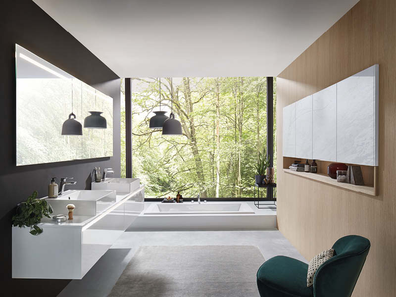 Modernes Nobilia Badezimmer mit Doppelwaschtisch in Weiß, freistehender Badewanne und großer Fensterfront, minimalistisch mit Holzdetails und Naturblick