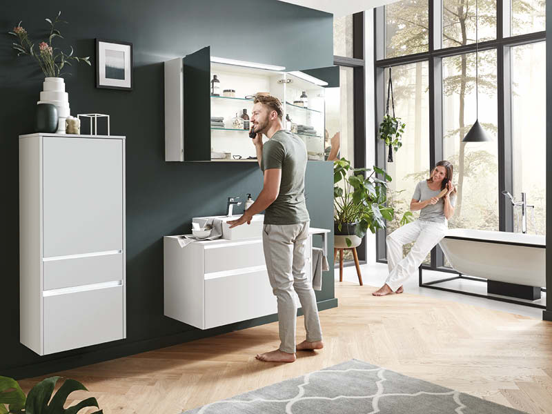 Durchdachte Badmöbel bei SPECHT: Nobilia Badezimmermöbel mit beleuchtetem Spiegelschrank, weißem Waschtisch und viel Stauraum, kombiniert mit grüner Wand und Holzfußboden