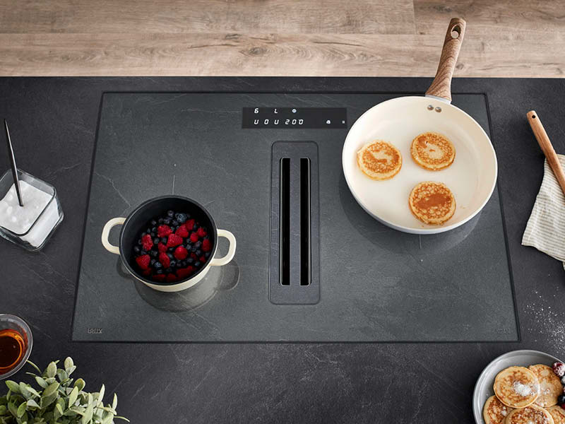 Induktionskochfeld mit integriertem Dunstabzug auf dunkler Arbeitsplatte, Pfanne und Topf beim Kochen, funktionale Küchentechnik