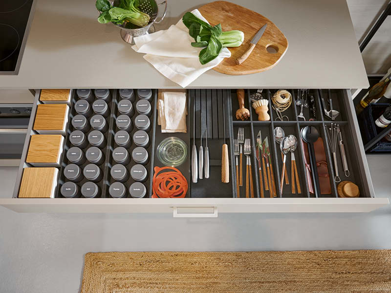 Geöffnete Küchenschublade mit Besteckeinsatz, Gewürzdosen, Messern und Utensilien für ergonomische Ordnung im Küchenalltag.
