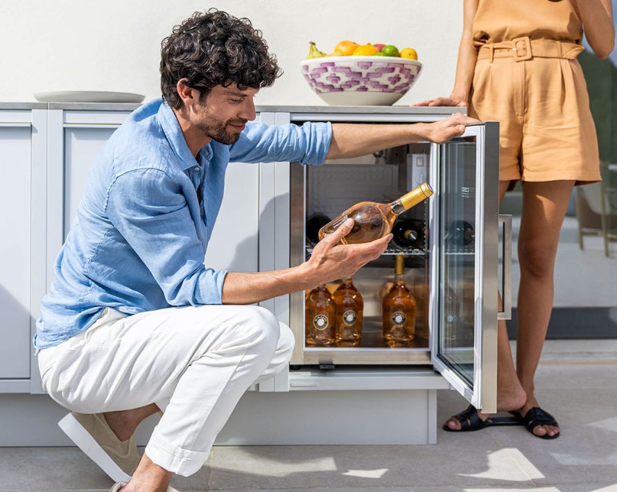 Mann holt Weinflasche aus Kühlschrank in einer Outdoor-Küche von BURN