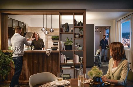 Offene Holzküche mit Gästen beim Kochen im Alltag, warmen Pendelleuchten, Esstisch und wohnlicher Kücheninsel für gesellige Abende.
