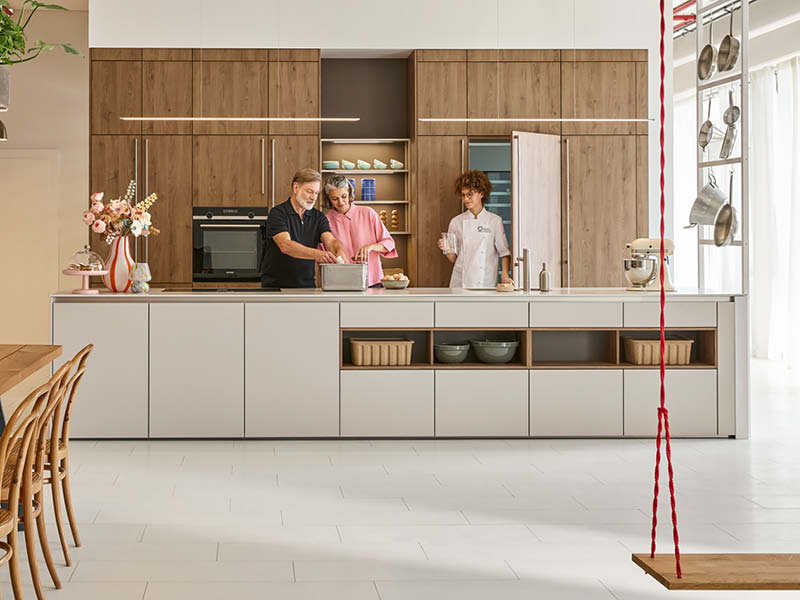 Helle Familienküche mit Holzfronten, großer Kücheninsel und drei Personen beim gemeinsamen Kochen im Alltag in moderner Wohnküche.