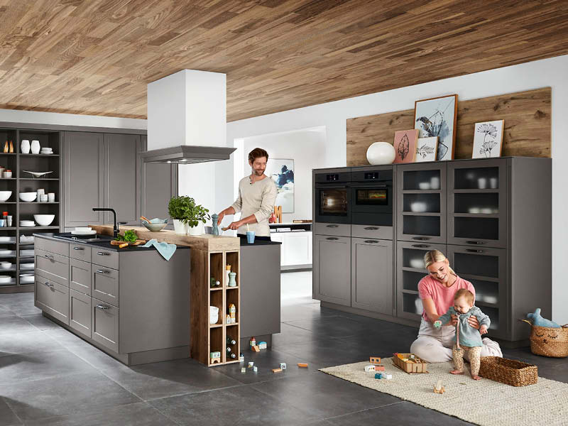 Großzügige Familienküche von nobilia mit grauen Fronten, Kochinsel und offenen Regalen aus Holz, die Kochen, Spielen und Wohnen harmonisch verbindet.