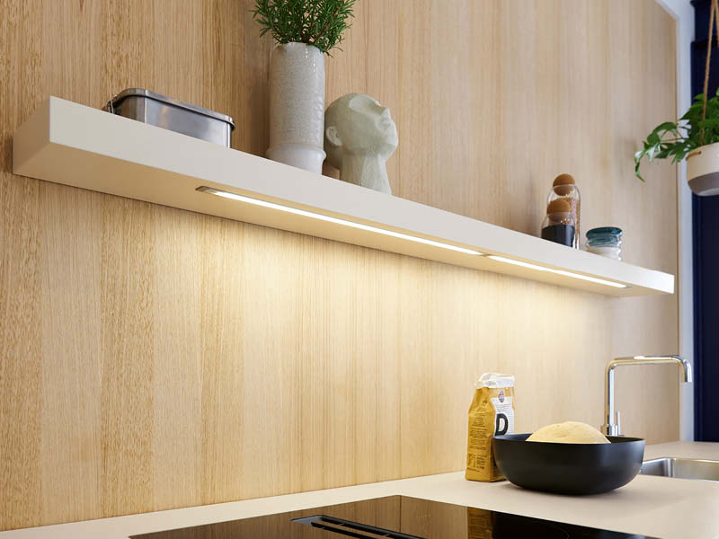 Schwebendes weißes Küchenregal mit integrierter LED-Unterbauleuchte beleuchtet Arbeitsplatte und Holzrückwand warm und blendfrei.