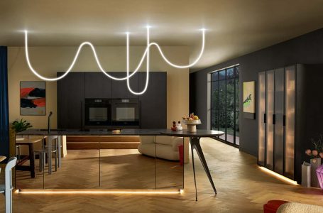 Moderne Küche mit dunkler Insel, warmen LED-Lichtleisten am Sockel und dekorativer Leuchte für stimmungsvolle Küchenbeleuchtung.
