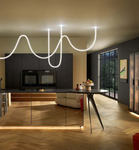 Moderne Küche mit dunkler Insel, warmen LED-Lichtleisten am Sockel und dekorativer Leuchte für stimmungsvolle Küchenbeleuchtung.