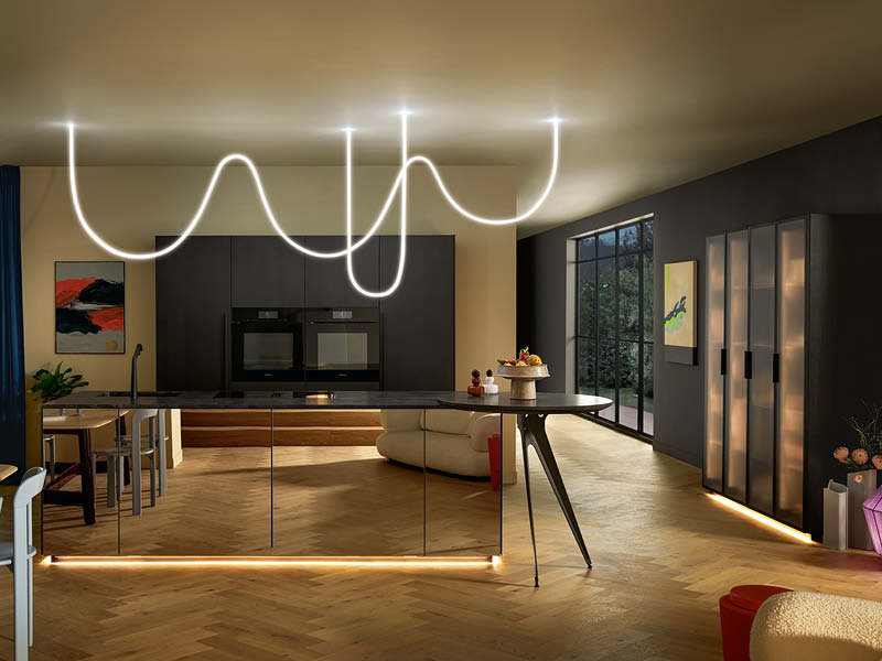 Moderne Küche mit dunkler Insel, warmen LED-Lichtleisten am Sockel und dekorativer Leuchte für stimmungsvolle Küchenbeleuchtung.