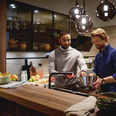Zwei Männer stehen in gemütlicher Küche von Schüller und bereiten Essen an der Spüle zu