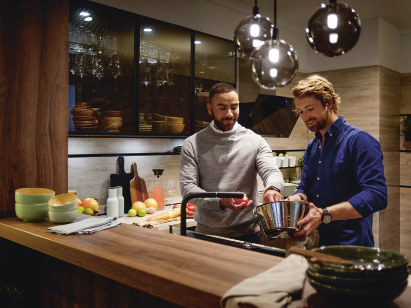 Zwei Männer stehen in gemütlicher Küche von Schüller und bereiten Essen an der Spüle zu