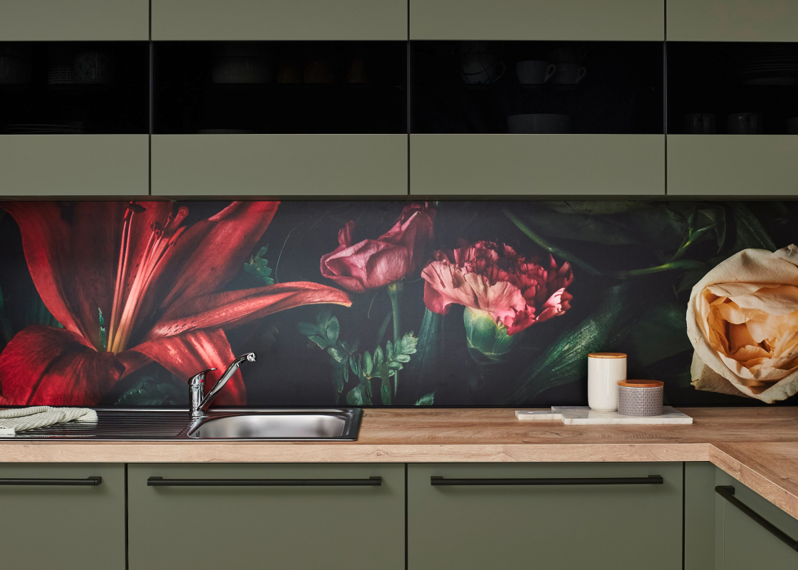 Küchenrückwand mit großen roten und cremefarbenen Blüten, kombiniert mit olivgrünen Fronten und einer Arbeitsplatte in Holzoptik.