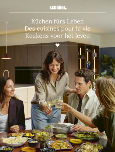 Cover des Schüller Küchenjournals 2027 „Küchen fürs Leben“: vier Personen stoßen beim gemeinsamen Essen in einer Küche an.