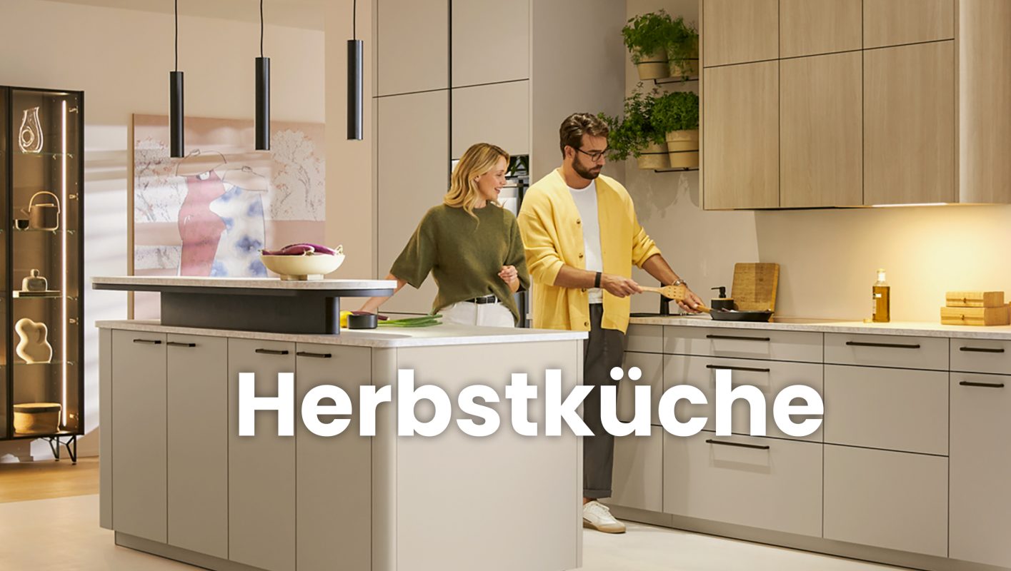 Paar beim gemeinsamen Kochen in einer modernen hellen Küche mit Kücheninsel, Holzfronten, Kräutern und warmen Naturtönen – stimmungsvolle Herbstküche.
